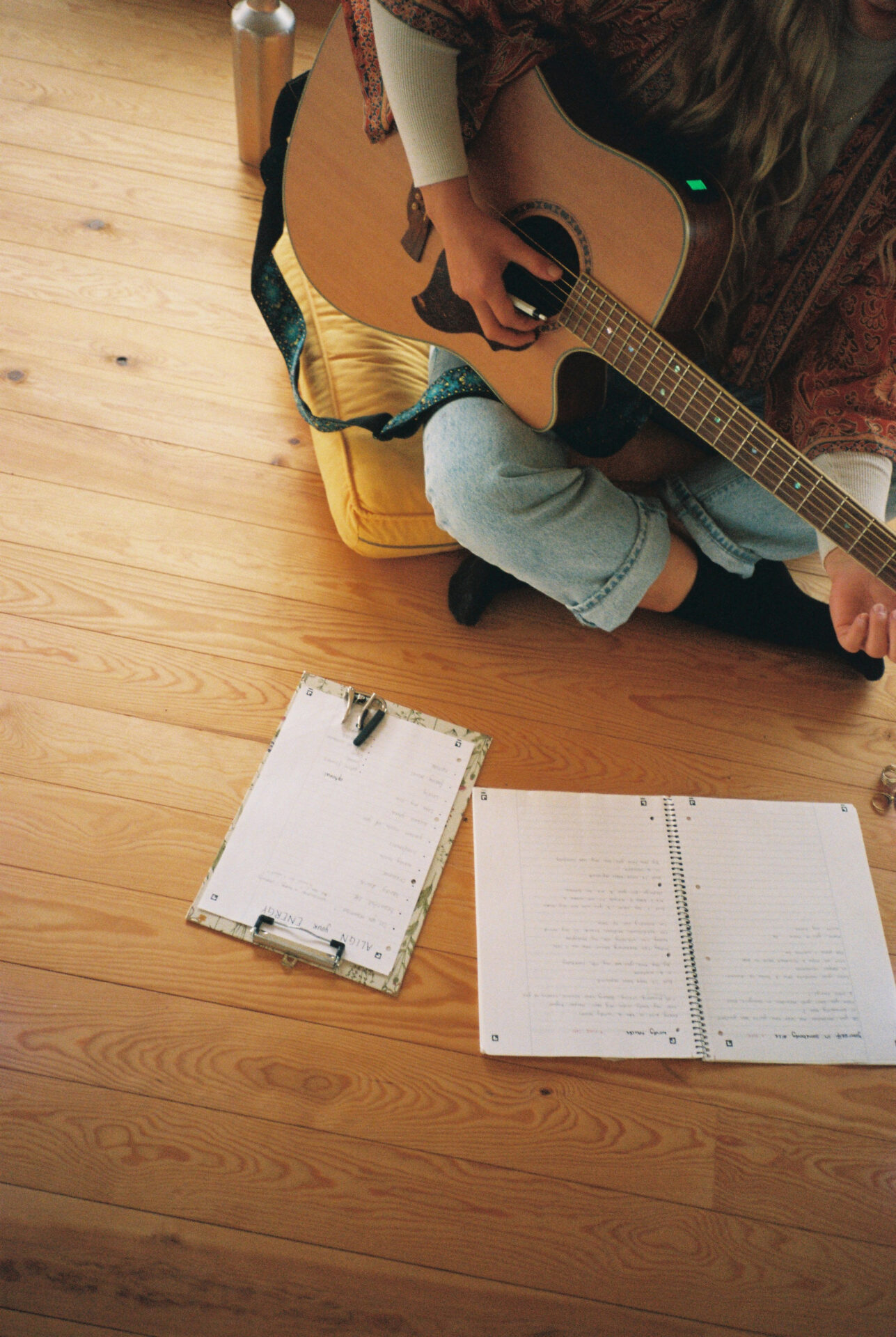 A girl sitting on the ground with a guitar, writing  notes about her future songs 