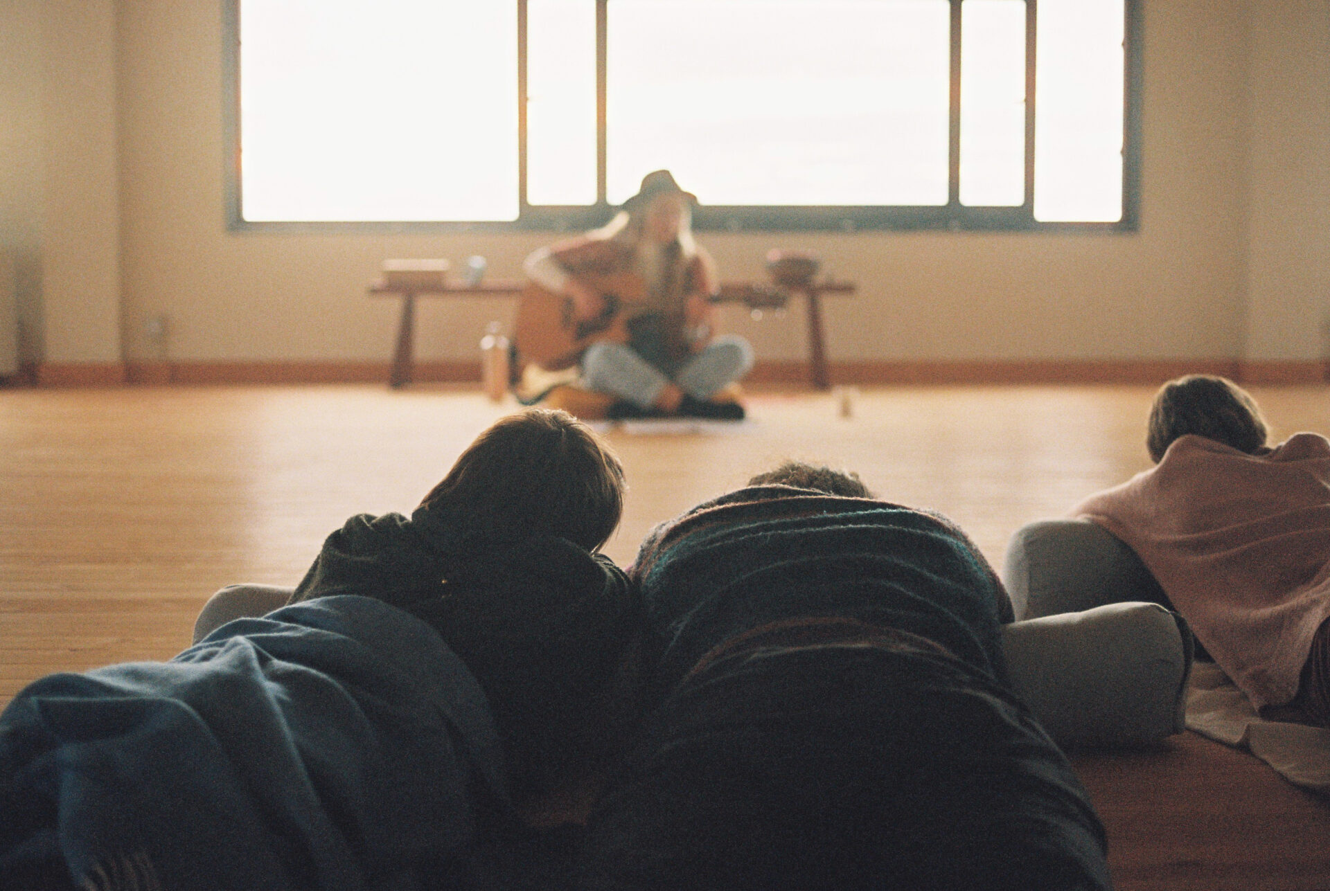 A couple fooled in the warm blanket is lying on the ground and watching a singer playing her own song songs.